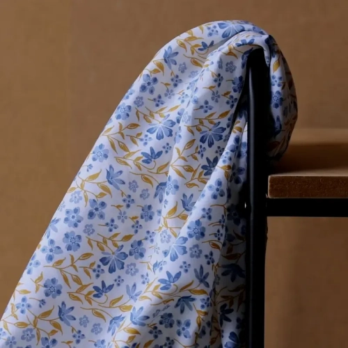 Niebieska popelina bawełniana Poppy Fabrics w gęsty wzór drobnych kwiatów i musztardowych listków o gładkim splocie.