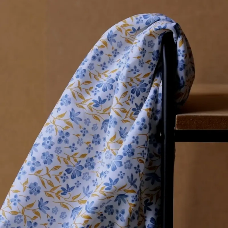 Niebieska popelina bawełniana Poppy Fabrics w gęsty wzór drobnych kwiatów i musztardowych listków o gładkim splocie.